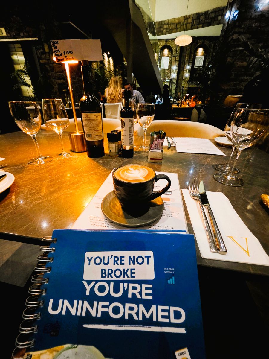 POV of the book: You're Not Broke. You're Uninformed by Author - Sakhile Mahlangu in your hand at a fancy cafe